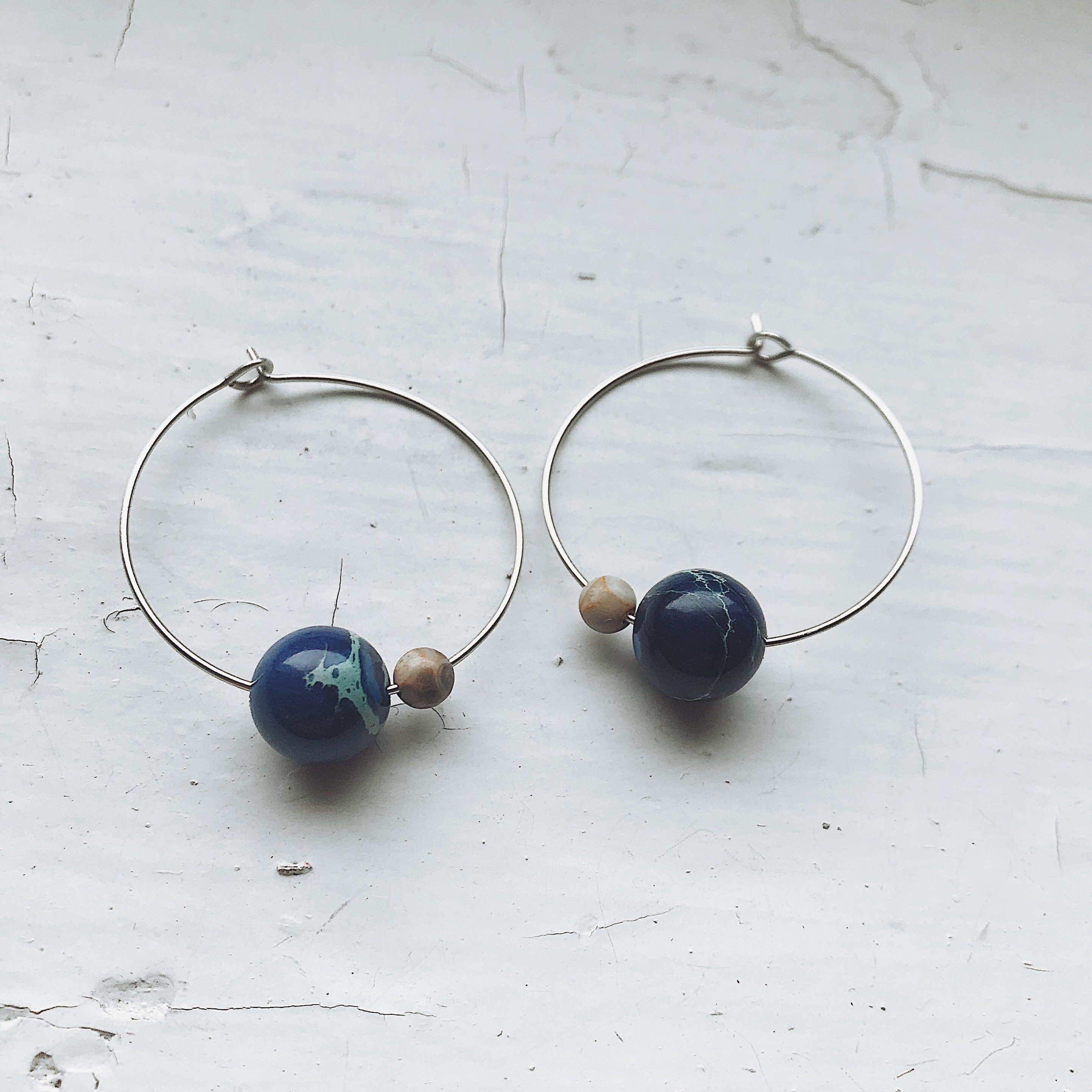 A pair of Earth and Moon Jasper Bead Hoop Earrings featuring colorful jasper beads on a raw brass hoop, showcasing a cosmic design.