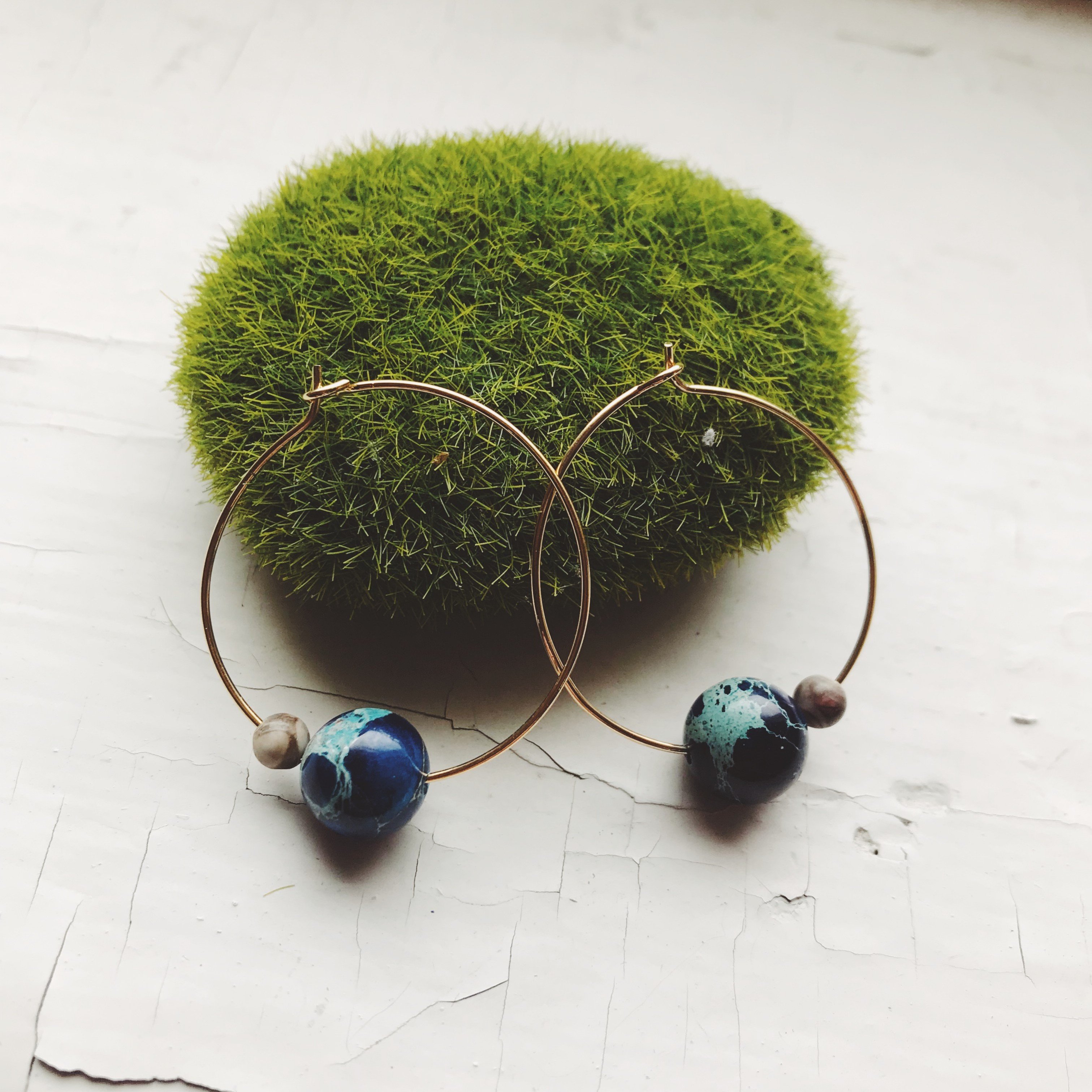 A pair of Earth and Moon Jasper Bead Hoop Earrings featuring colorful jasper beads on a raw brass hoop, showcasing a cosmic design.