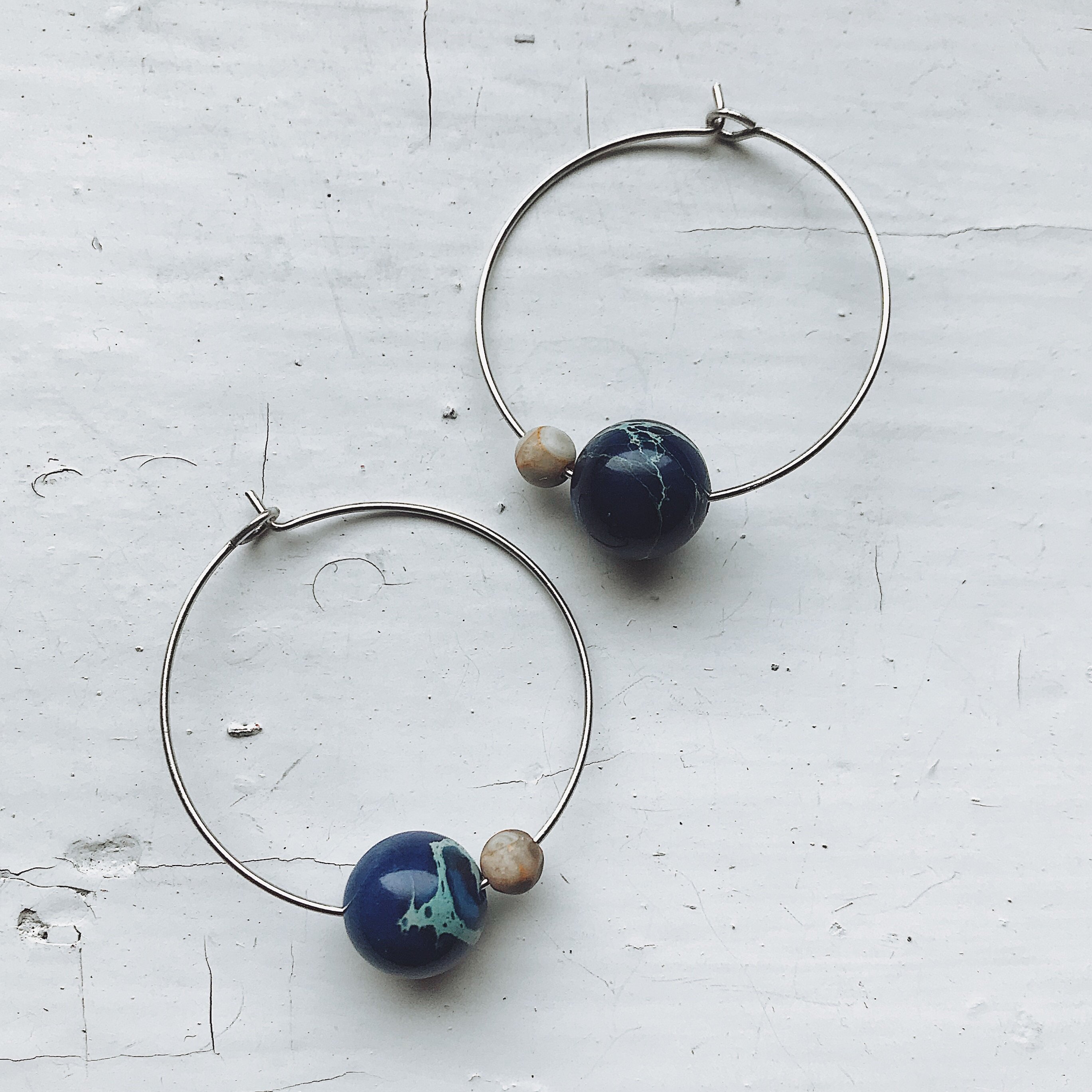 A pair of Earth and Moon Jasper Bead Hoop Earrings featuring colorful jasper beads on a raw brass hoop, showcasing a cosmic design.