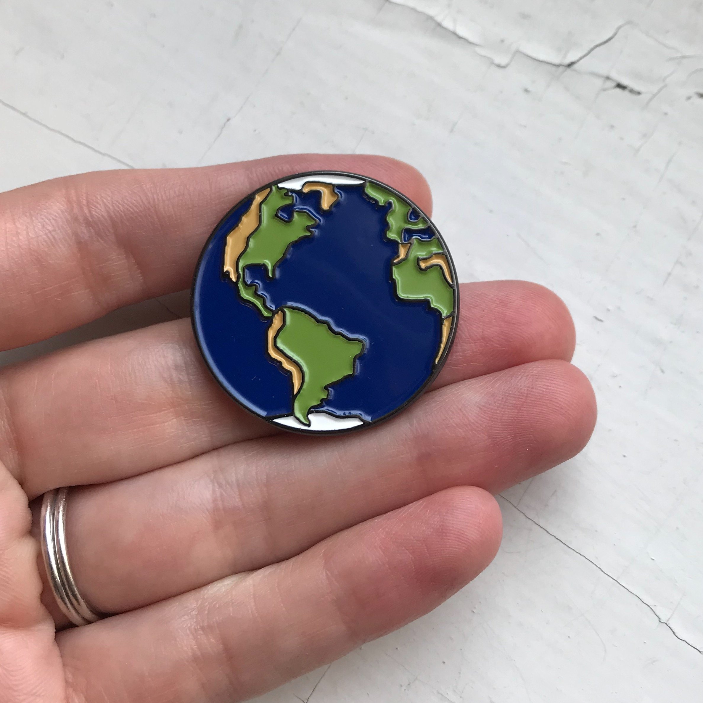 A colorful Earth Enamel Pin featuring a vibrant blue planet design, perfect for jackets and backpacks.