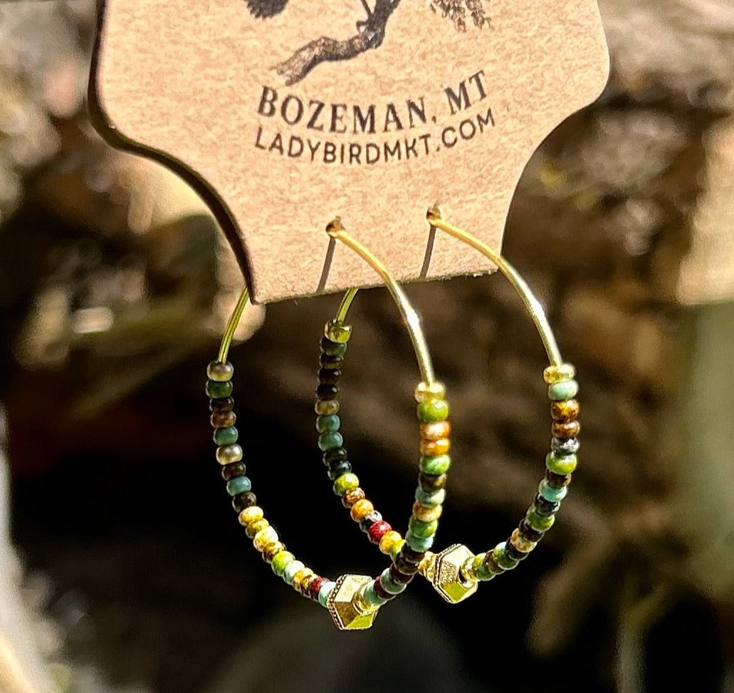 A pair of Earthy Greens & Gold Beaded Hoop Earrings featuring vibrant green and brown seed beads on a gold hoop.