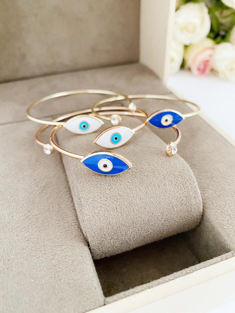 Elegant gold cuff bracelet featuring a movable evil eye charm, showcasing intricate design and customizable colors.