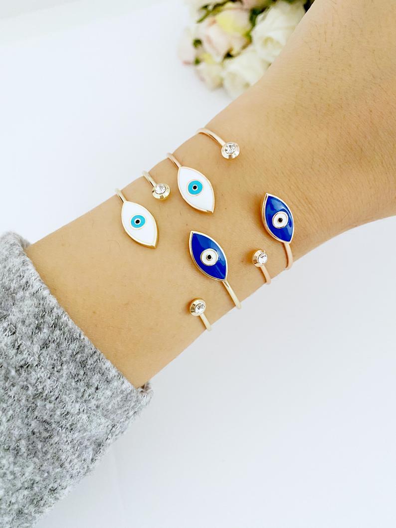 Elegant gold cuff bracelet featuring a movable evil eye charm, showcasing intricate design and customizable colors.