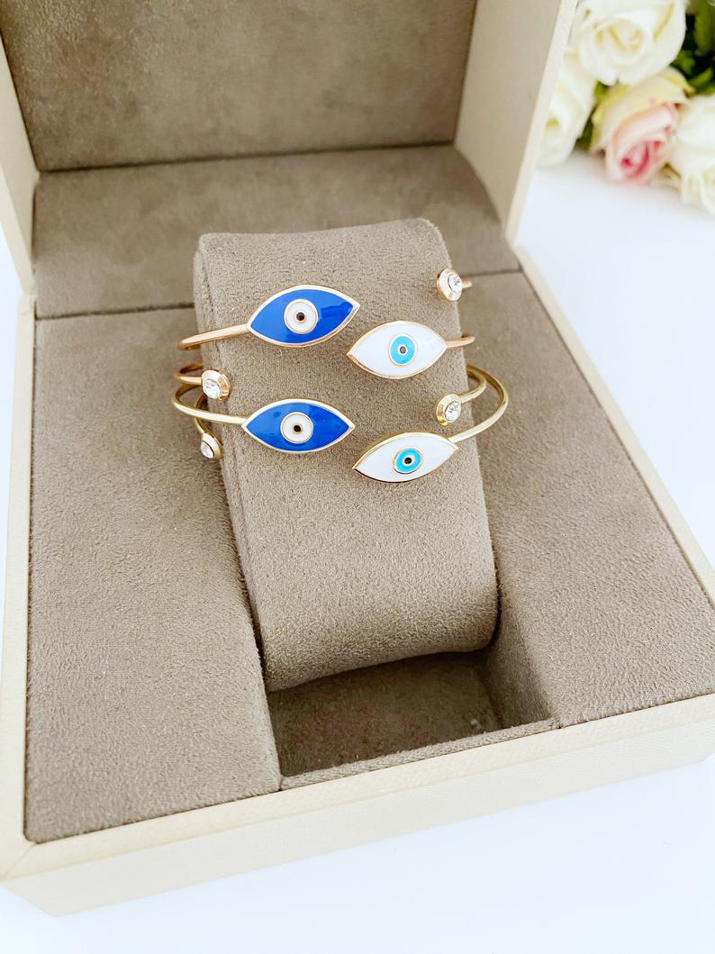 Elegant gold cuff bracelet featuring a movable evil eye charm, showcasing intricate design and customizable colors.