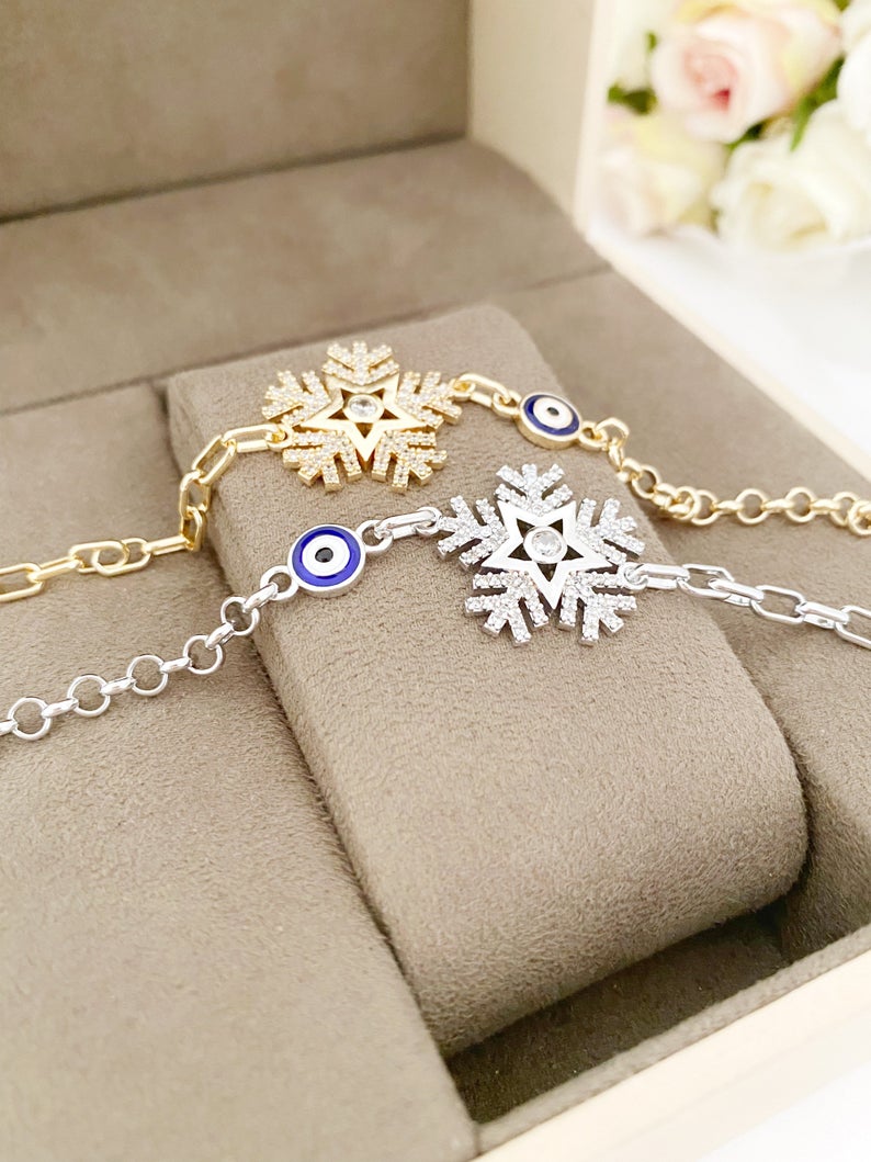 Elegant Evil Eye Chain Bracelet featuring a blue evil eye, snowflake charm, and clover charm, available in gold and silver finishes.