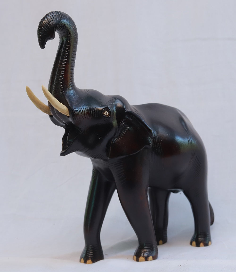 Handcrafted wooden elephant sculpture with trunk raised, symbolizing good luck and protection, intricately carved by skilled artisans from Kerala, India.