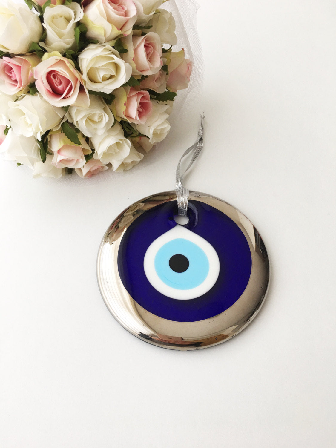 A beautifully handcrafted 13cm Evil Eye Bead with silver trim, featuring a vibrant blue color and a blue rope for hanging.