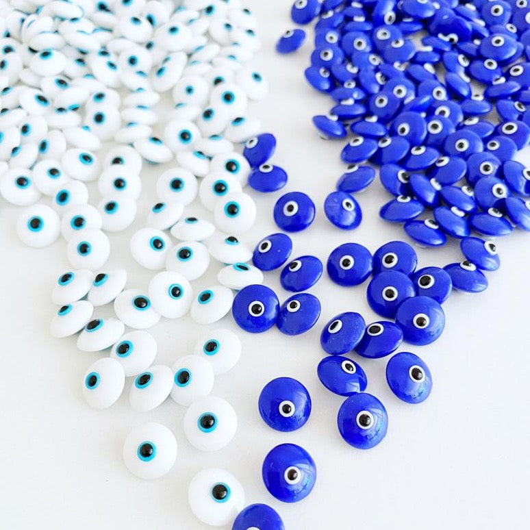 A collection of glass evil eye beads in white and blue colors, showcasing their intricate designs and vibrant hues, perfect for jewelry making.