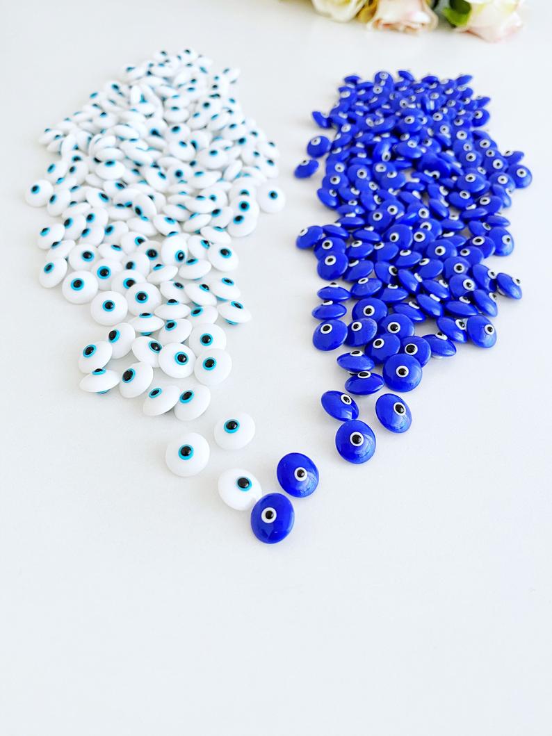 A collection of glass evil eye beads in white and blue colors, showcasing their intricate designs and vibrant hues, perfect for jewelry making.