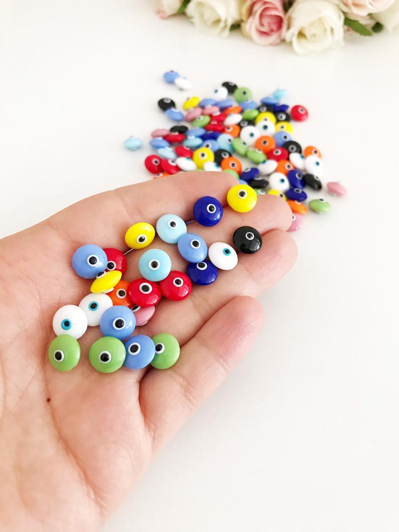 A collection of glass evil eye beads in white and blue colors, showcasing their intricate designs and vibrant hues, perfect for jewelry making.