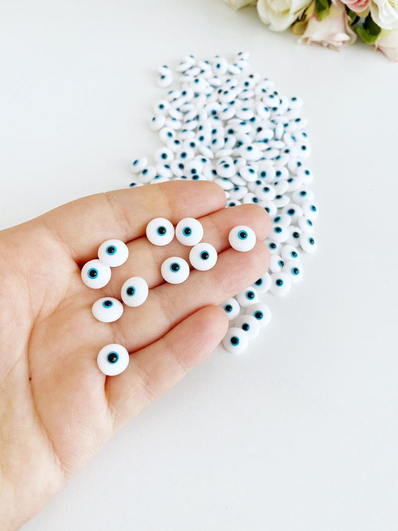 A collection of glass evil eye beads in white and blue colors, showcasing their intricate designs and vibrant hues, perfect for jewelry making.