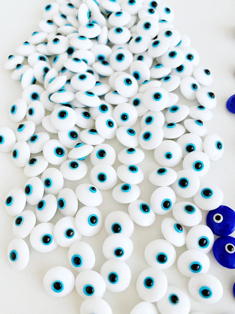 A collection of glass evil eye beads in white and blue colors, showcasing their intricate designs and vibrant hues, perfect for jewelry making.