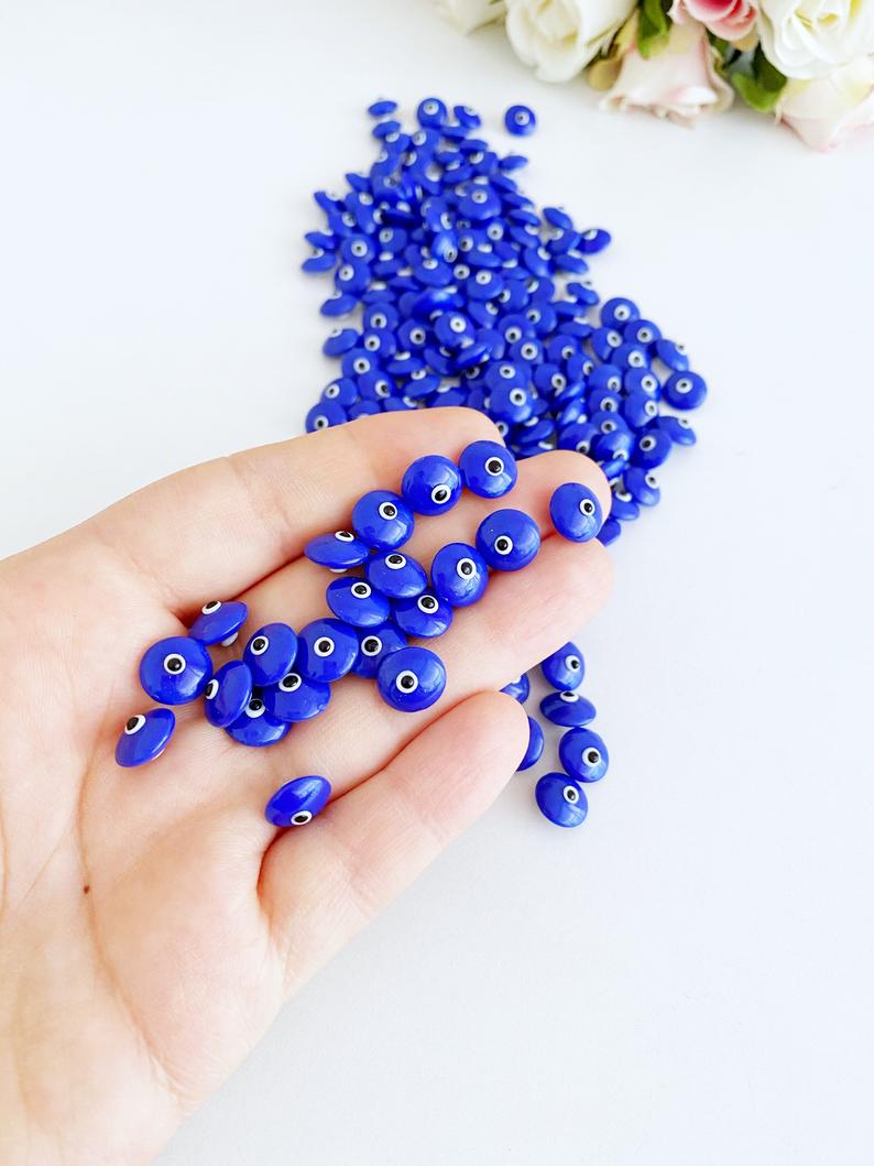 A collection of glass evil eye beads in white and blue colors, showcasing their intricate designs and vibrant hues, perfect for jewelry making.