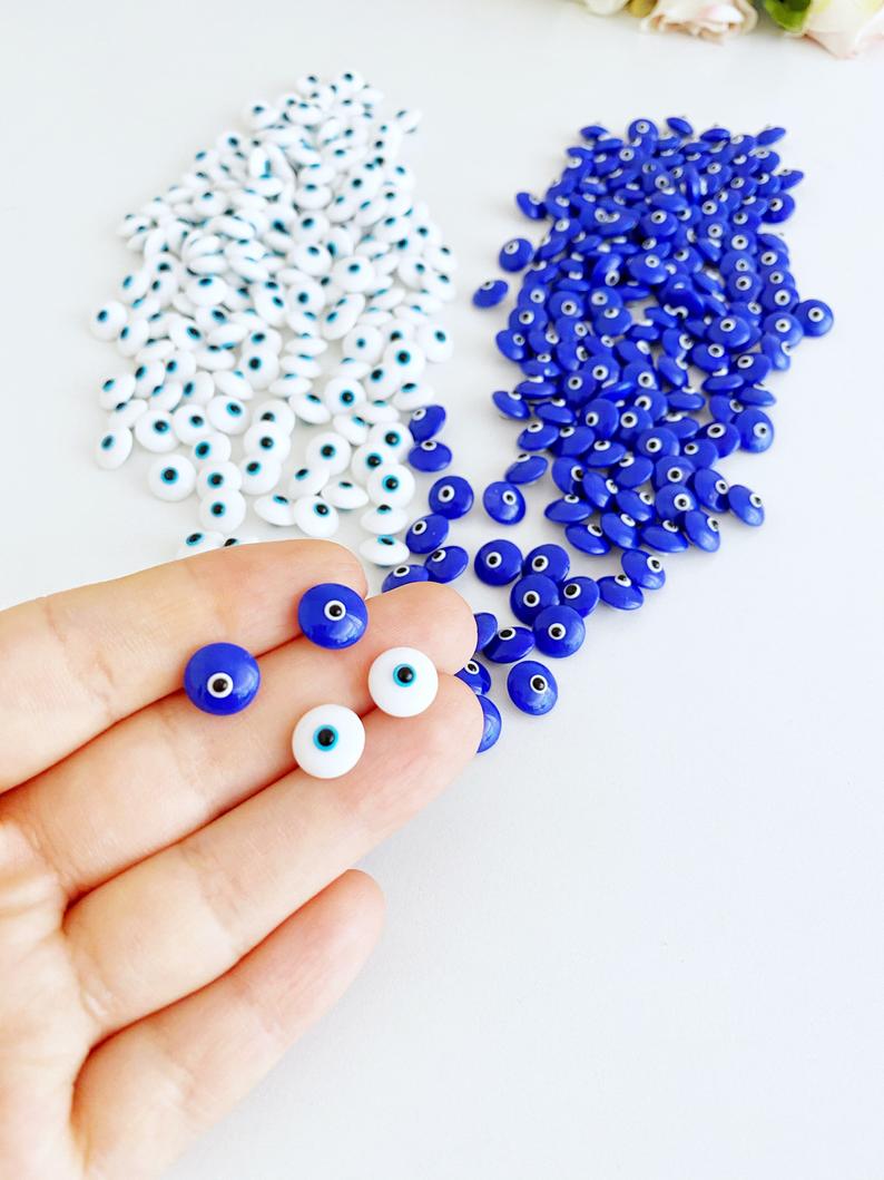 A collection of glass evil eye beads in white and blue colors, showcasing their intricate designs and vibrant hues, perfect for jewelry making.