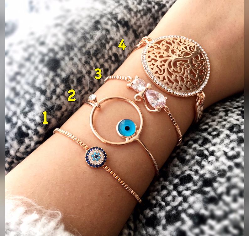 A beautiful rose gold Evil Eye Bracelet set featuring various designs including a tiny evil eye bead, bangle, adjustable cat, and tree of life bracelet.