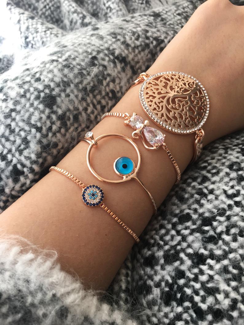 A beautiful rose gold Evil Eye Bracelet set featuring various designs including a tiny evil eye bead, bangle, adjustable cat, and tree of life bracelet.