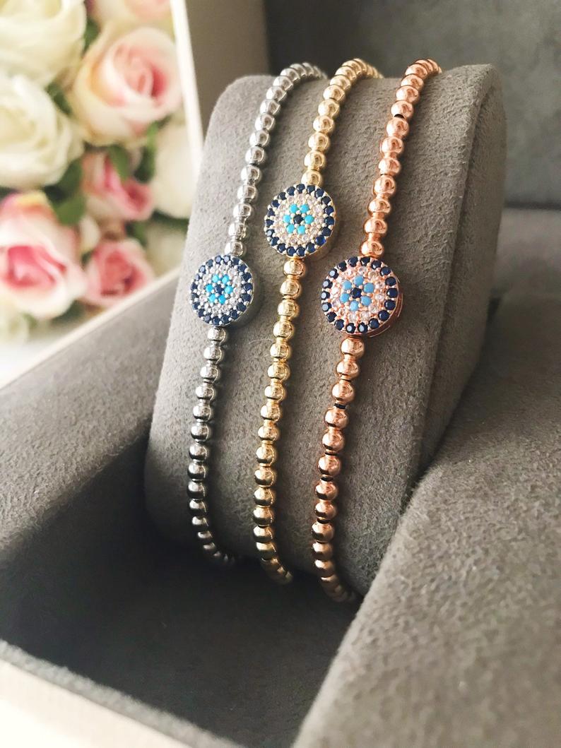 A stylish Evil Eye Bracelet featuring a beaded design with an adjustable string, available in silver and rose gold, made from tarnish-resistant stainless steel.