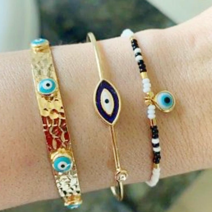 A beautiful Evil Eye Bracelet featuring seed beads and a gold finish, showcasing various styles including a turquoise cuff and blue oval bangle.