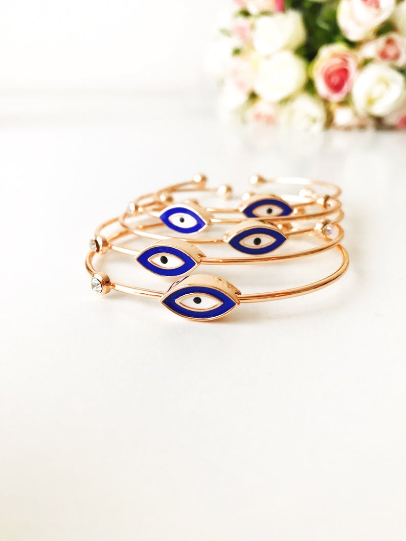 A beautiful Evil Eye Bracelet featuring seed beads and a gold finish, showcasing various styles including a turquoise cuff and blue oval bangle.