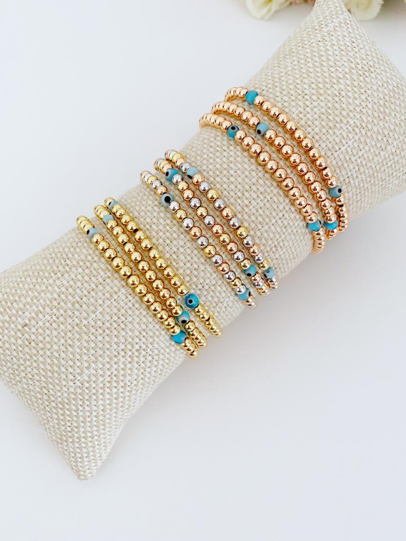 Elegant Evil Eye Bracelet featuring gold balls and a protective charm, available in gold, rose gold, and mixed colors.