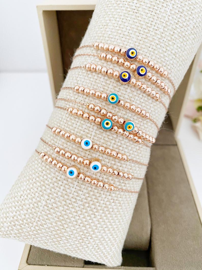 A stunning rose gold Evil Eye Bracelet featuring a minimalist design with a blue, white, or green evil eye charm, adjustable and handmade.