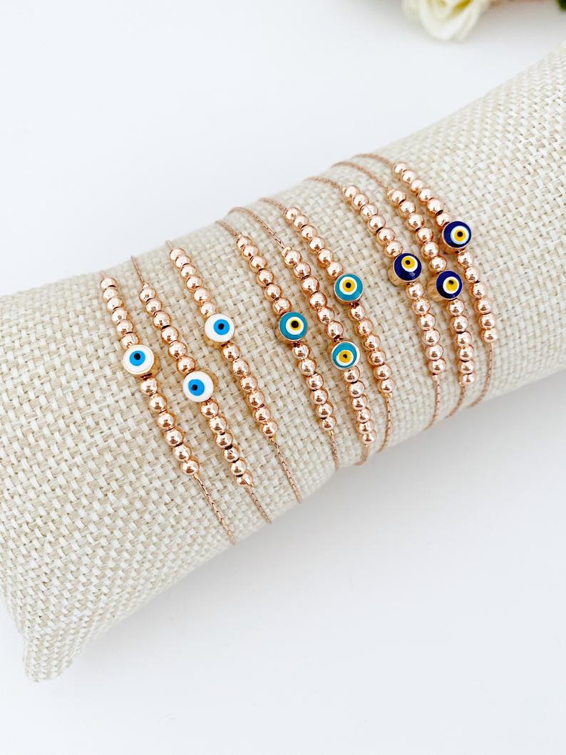 A stunning rose gold Evil Eye Bracelet featuring a minimalist design with a blue, white, or green evil eye charm, adjustable and handmade.