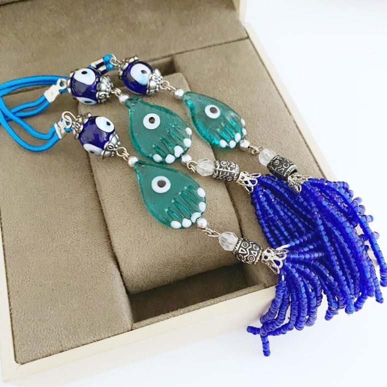 Handmade Evil Eye Car Charm featuring a Hamsa Hand design, made of glass beads, hanging from a rearview mirror.