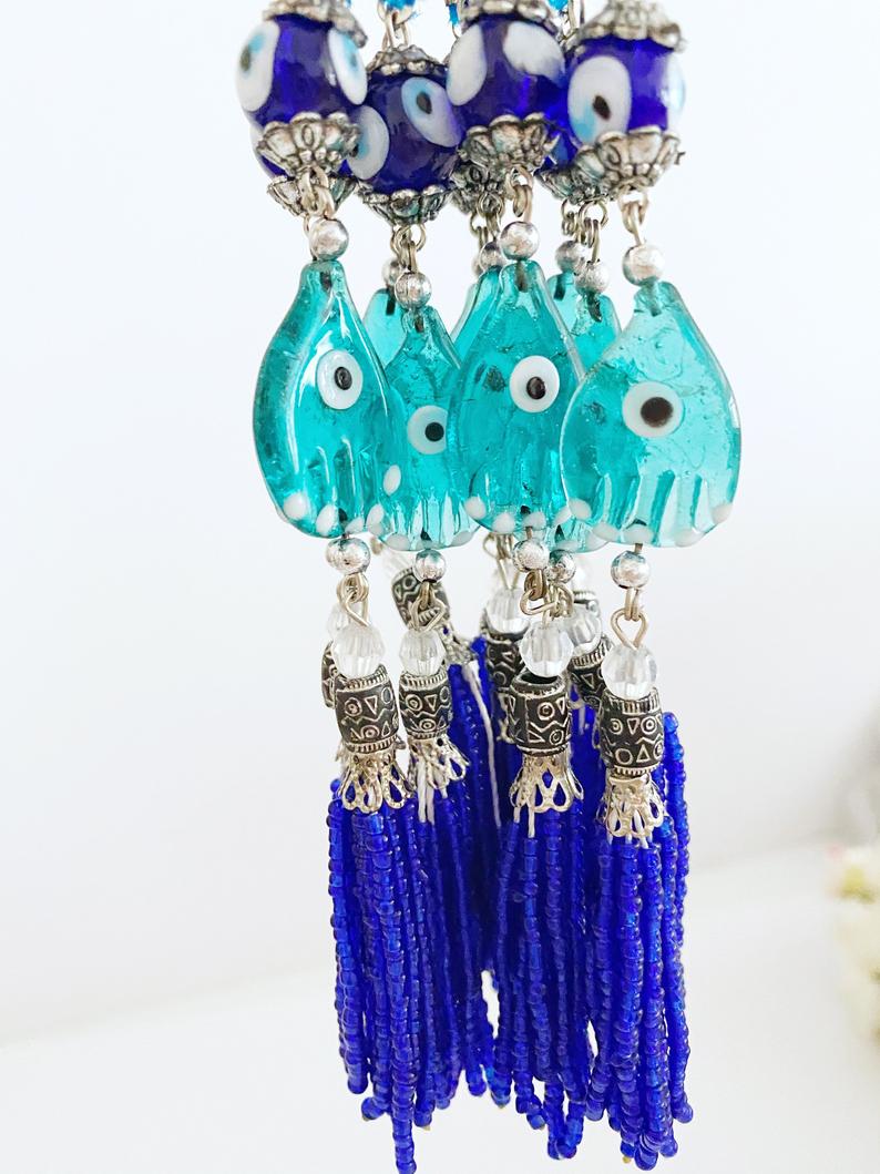 Handmade Evil Eye Car Charm featuring a Hamsa Hand design, made of glass beads, hanging from a rearview mirror.