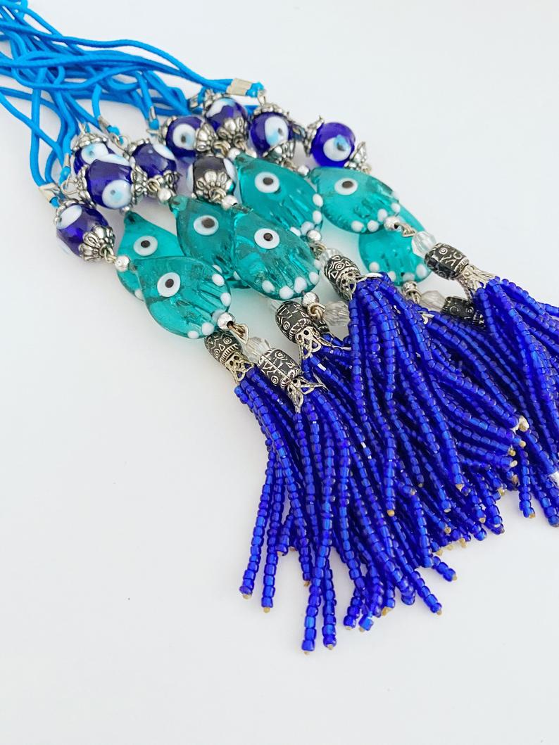 Handmade Evil Eye Car Charm featuring a Hamsa Hand design, made of glass beads, hanging from a rearview mirror.