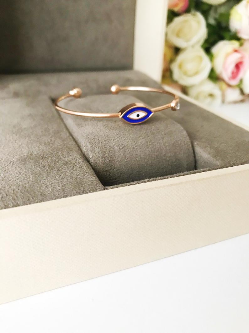 Evil Eye Cuff Bracelet featuring a movable blue and white charm on a rose gold bangle, showcasing its elegant design and adjustable size.