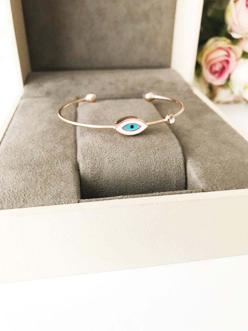 Evil Eye Cuff Bracelet featuring a movable blue and white charm on a rose gold bangle, showcasing its elegant design and adjustable size.