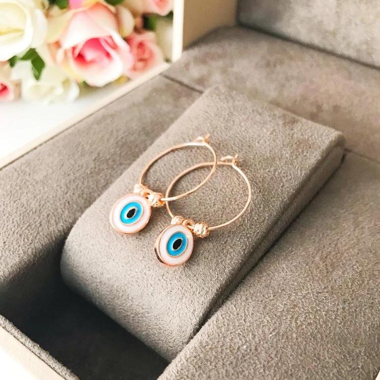 A pair of elegant evil eye dangle earrings featuring white hoops and blue evil eye beads, showcasing a unique handmade design.