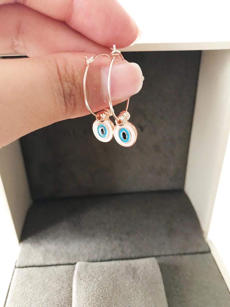 A pair of elegant evil eye dangle earrings featuring white hoops and blue evil eye beads, showcasing a unique handmade design.