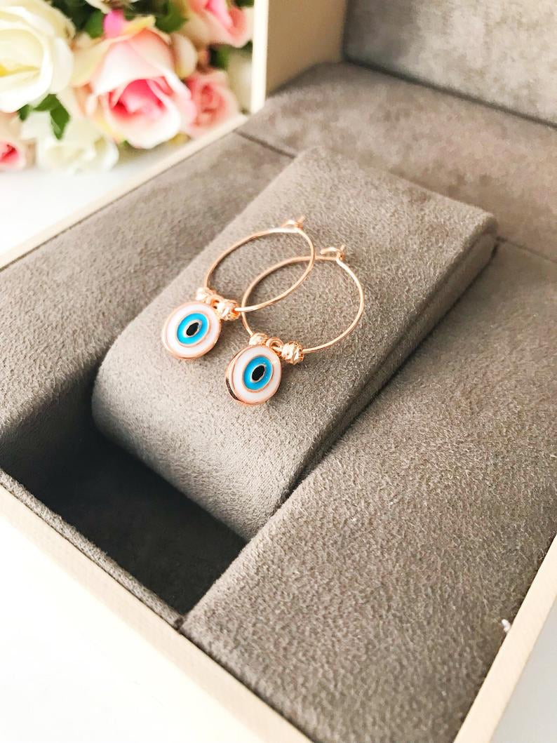 A pair of elegant evil eye dangle earrings featuring white hoops and blue evil eye beads, showcasing a unique handmade design.