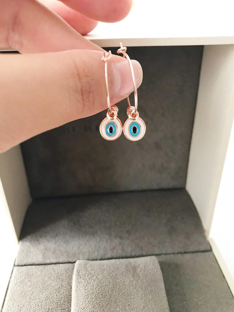 A pair of elegant evil eye dangle earrings featuring white hoops and blue evil eye beads, showcasing a unique handmade design.