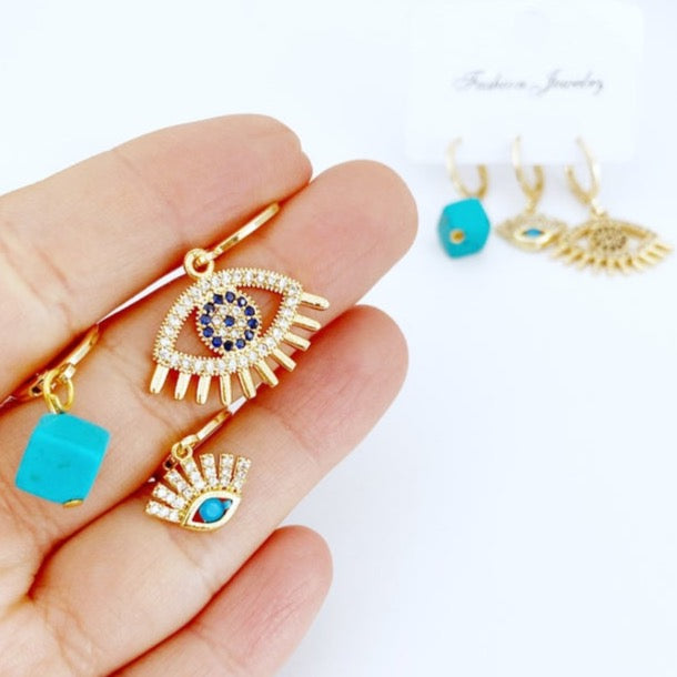 A set of three handmade gold hoop earrings featuring blue evil eye beads and zircon charms, showcasing a boho style.