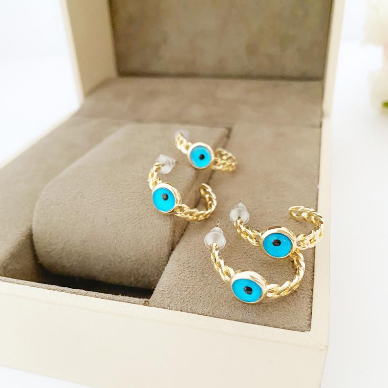 A pair of handmade chunky gold hoop earrings featuring a dainty blue evil eye bead, symbolizing protection and style.