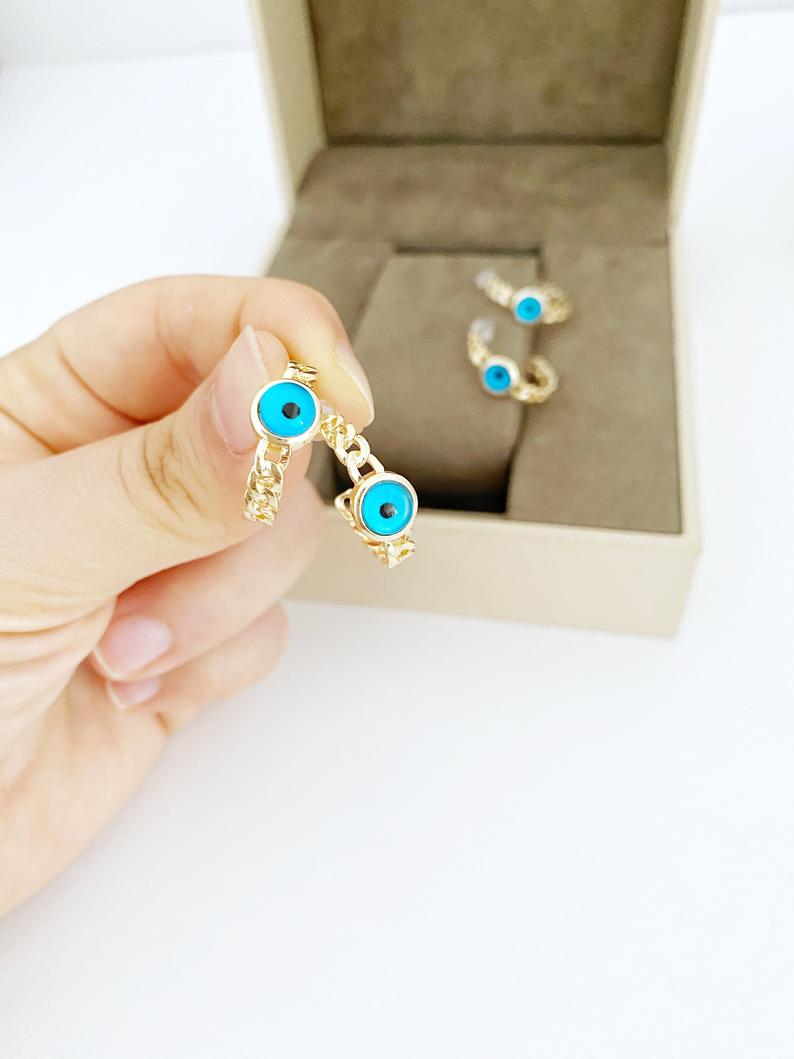 A pair of handmade chunky gold hoop earrings featuring a dainty blue evil eye bead, symbolizing protection and style.