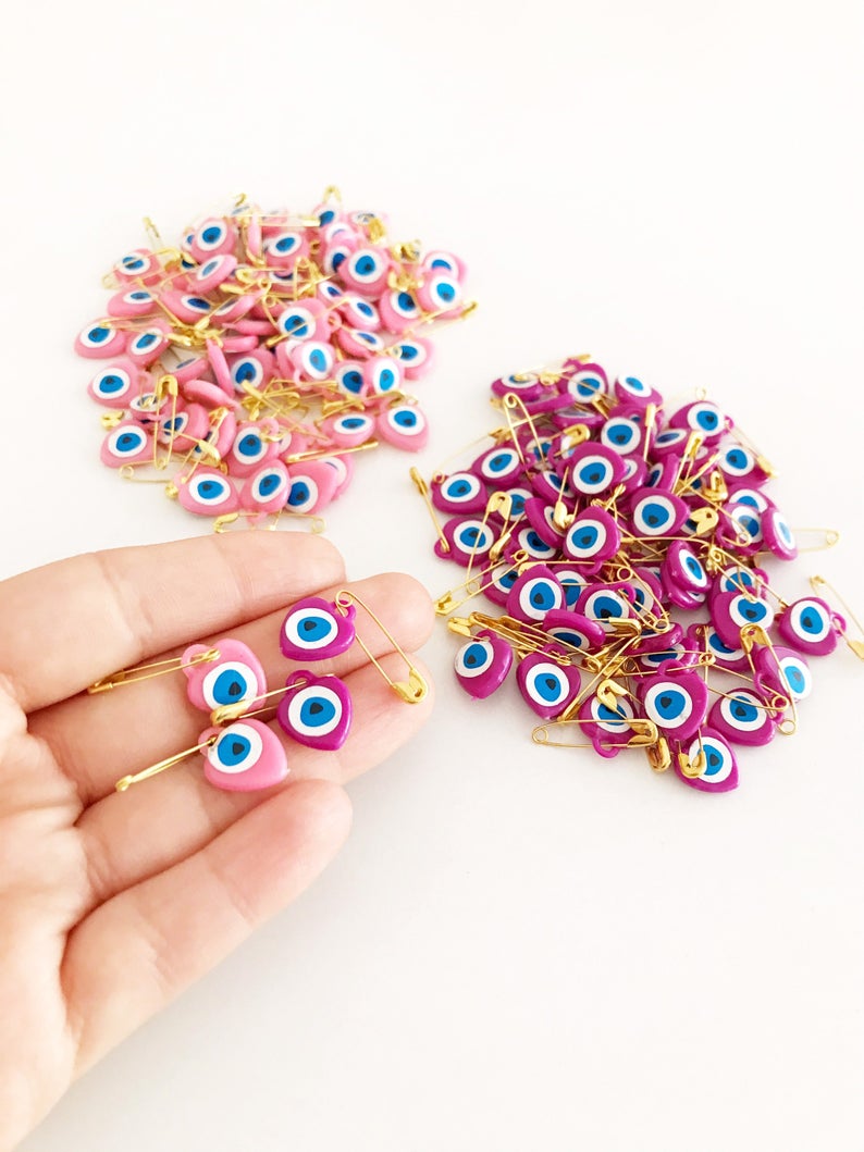 A collection of 100 pink evil eye safety pins featuring heart-shaped plastic beads with evil eye stickers, perfect for protection and gifting.