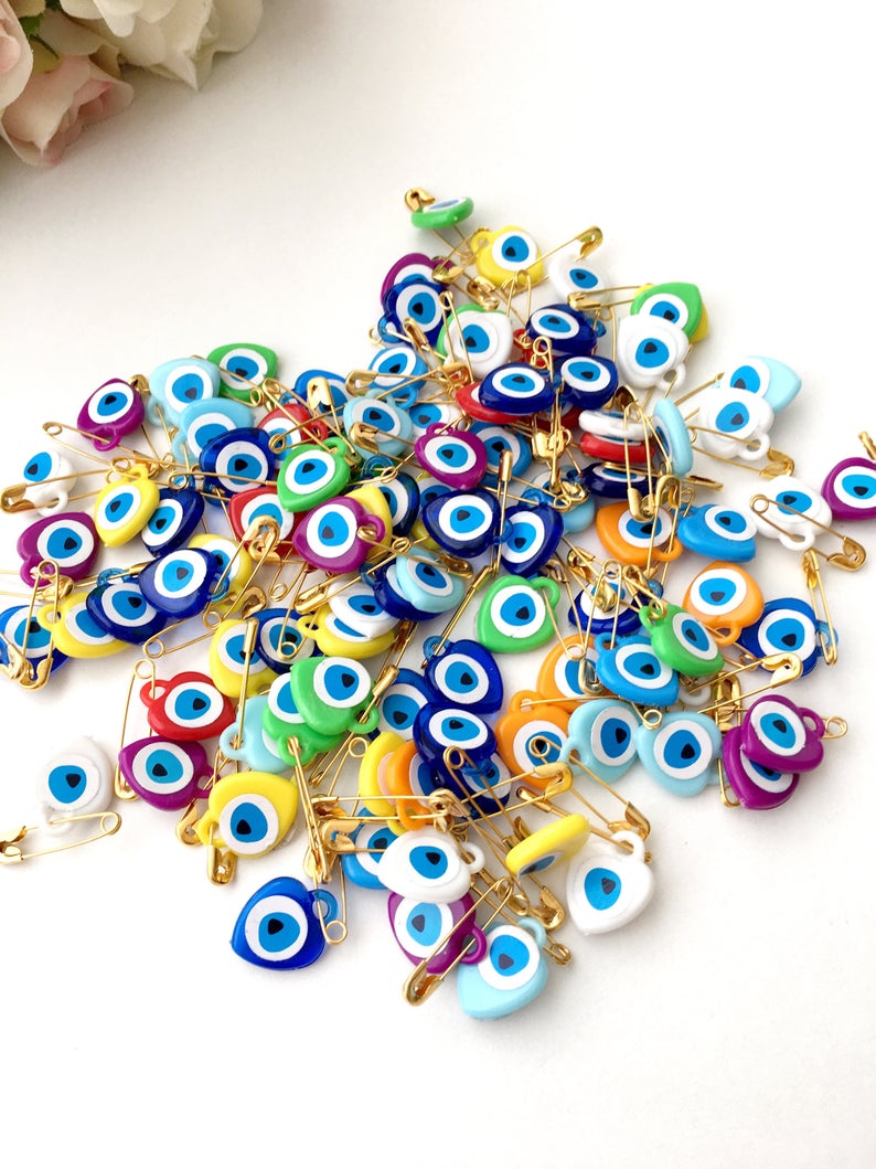 A collection of 100 pink evil eye safety pins featuring heart-shaped plastic beads with evil eye stickers, perfect for protection and gifting.