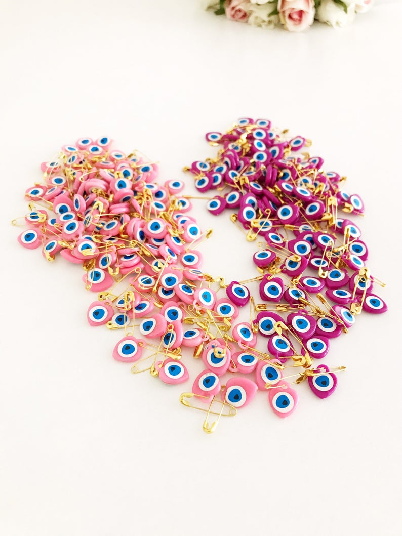 A collection of 100 pink evil eye safety pins featuring heart-shaped plastic beads with evil eye stickers, perfect for protection and gifting.