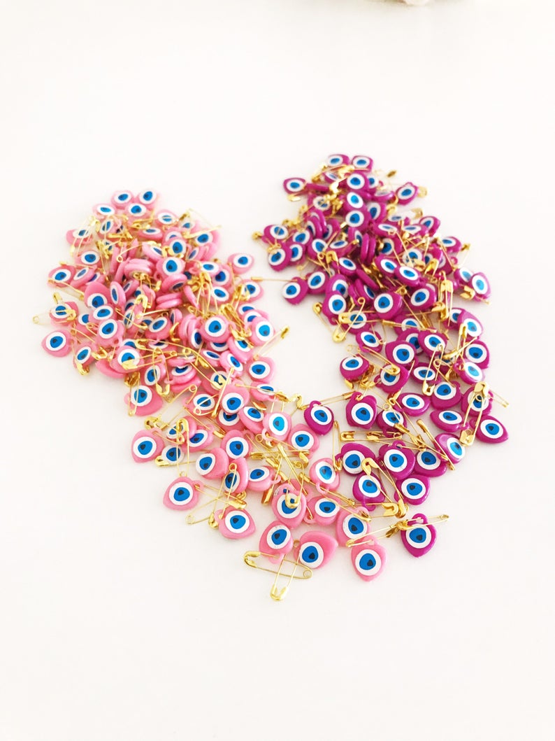 A collection of 100 pink evil eye safety pins featuring heart-shaped plastic beads with evil eye stickers, perfect for protection and gifting.