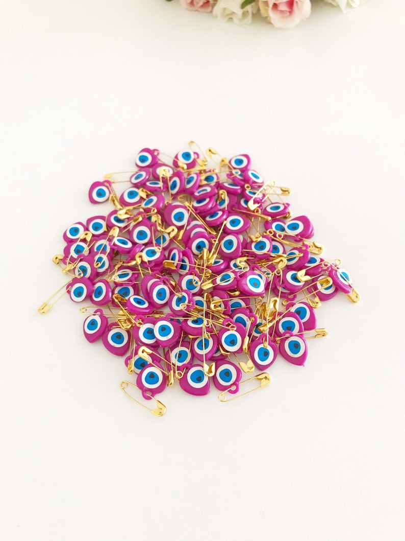 A collection of 100 pink evil eye safety pins featuring heart-shaped plastic beads with evil eye stickers, perfect for protection and gifting.