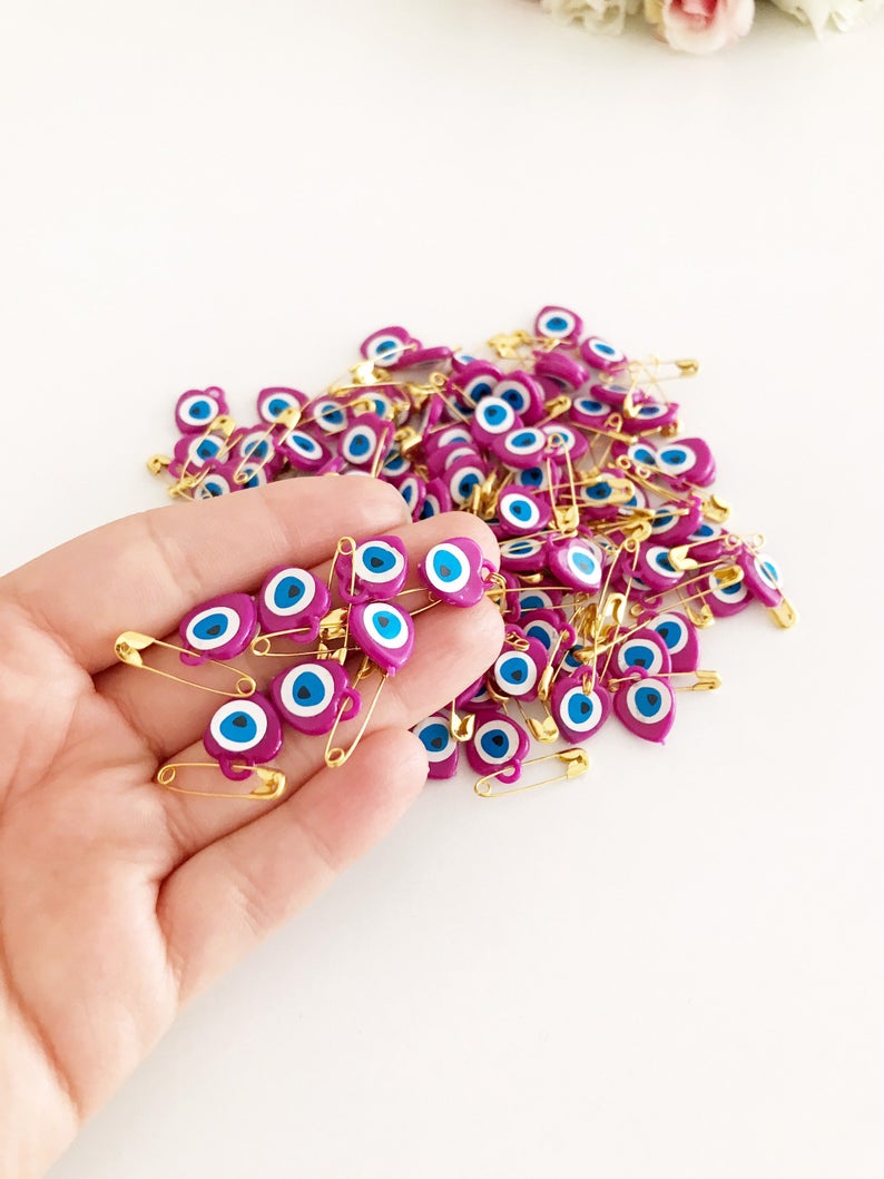 A collection of 100 pink evil eye safety pins featuring heart-shaped plastic beads with evil eye stickers, perfect for protection and gifting.