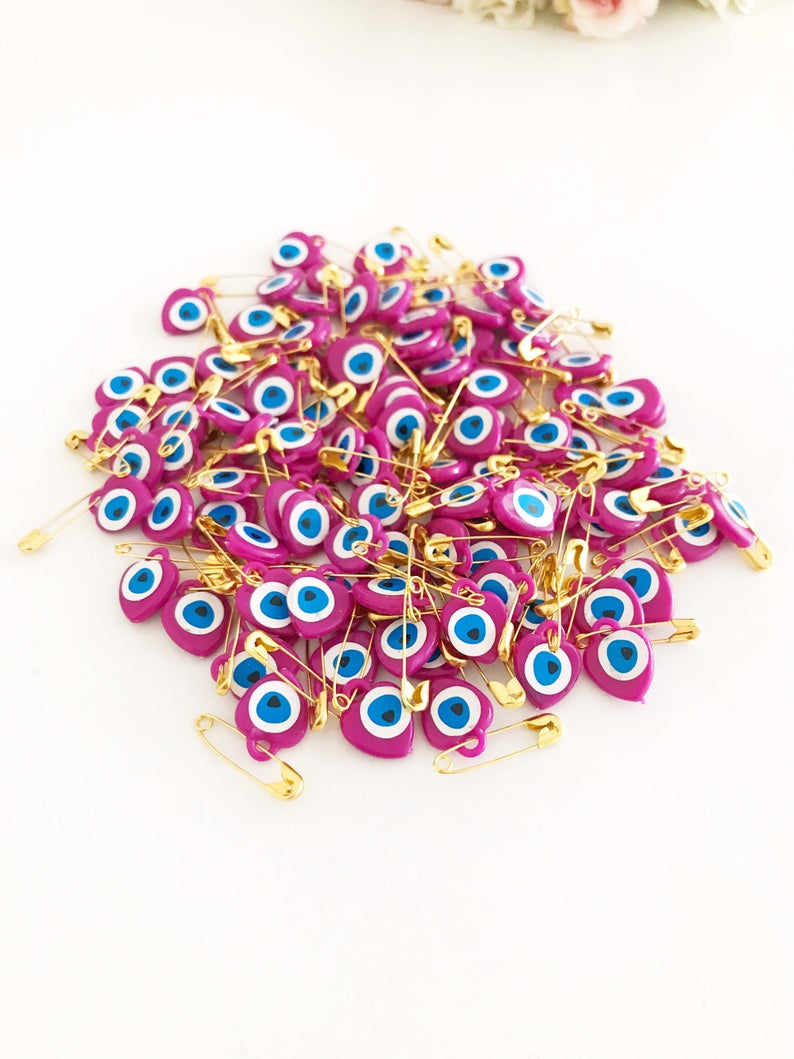 A collection of 100 pink evil eye safety pins featuring heart-shaped plastic beads with evil eye stickers, perfect for protection and gifting.