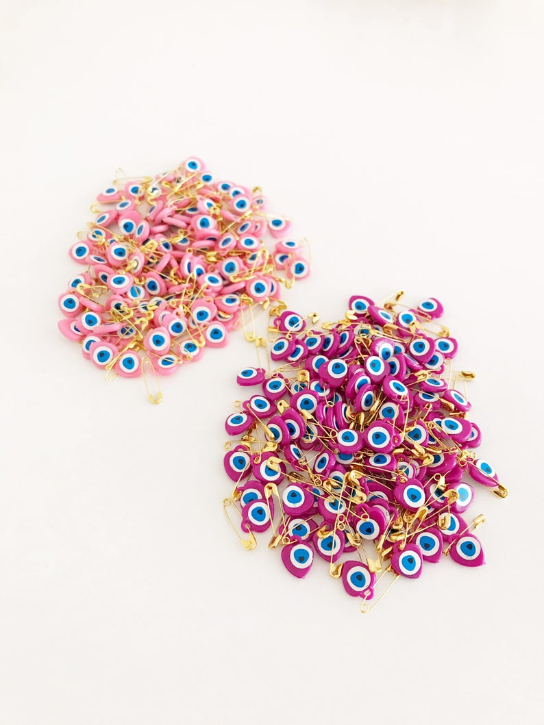 A collection of 100 pink evil eye safety pins featuring heart-shaped plastic beads with evil eye stickers, perfect for protection and gifting.