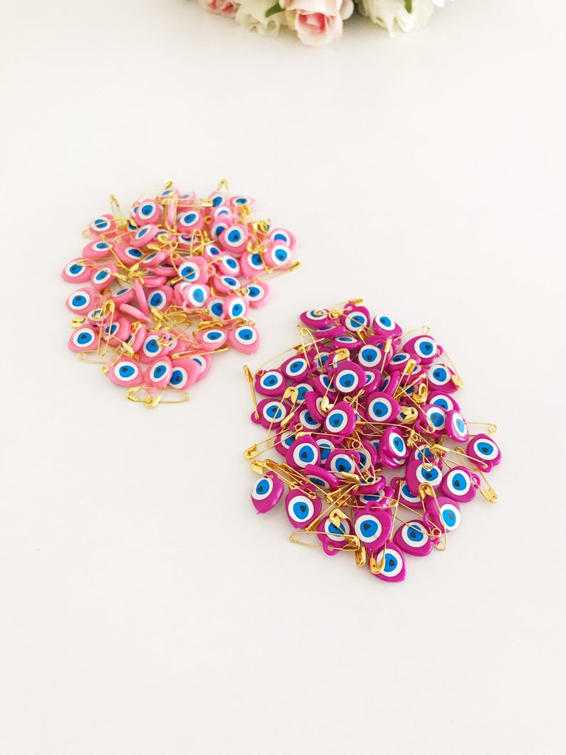 A collection of 100 pink evil eye safety pins featuring heart-shaped plastic beads with evil eye stickers, perfect for protection and gifting.