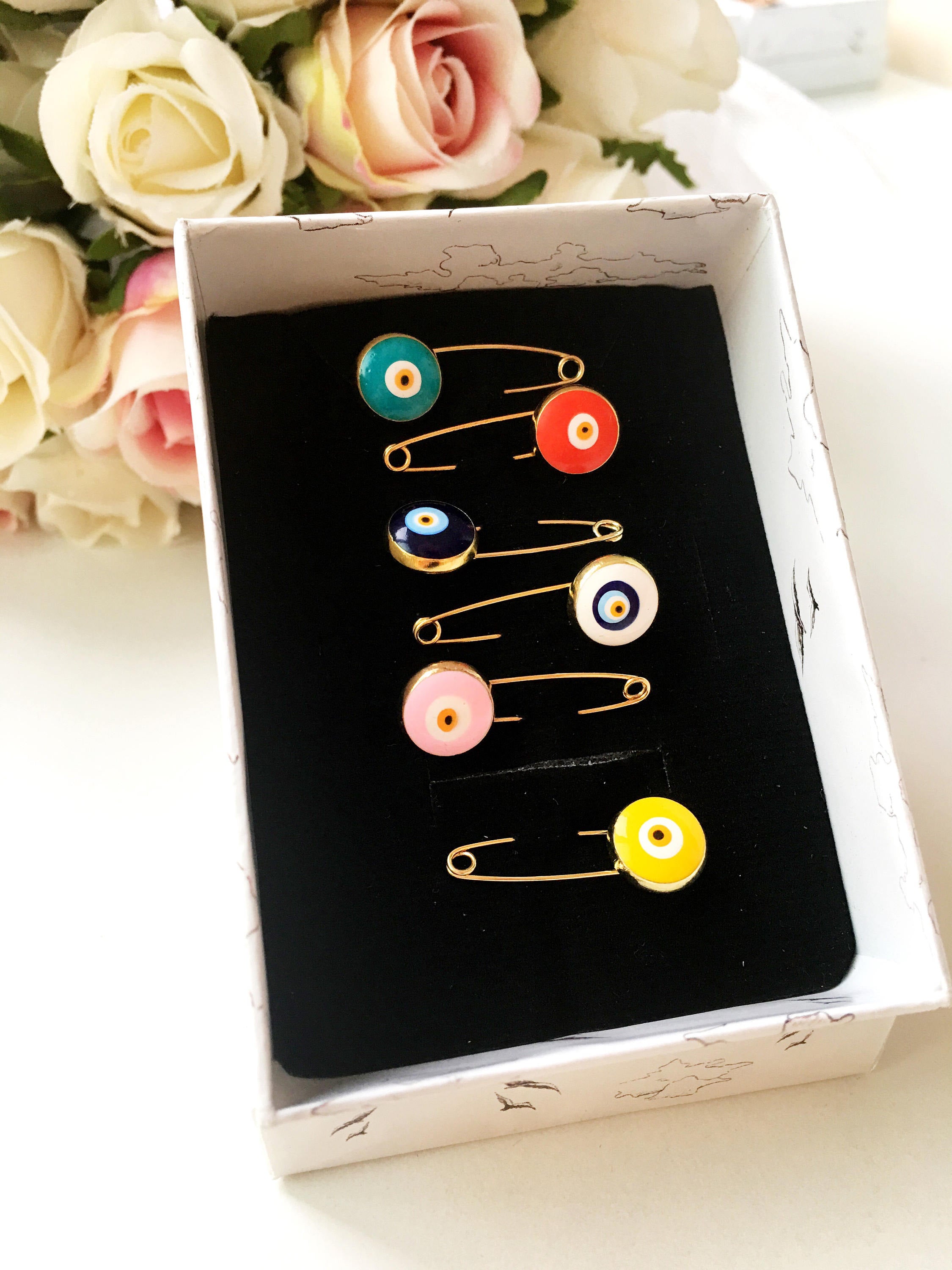 Gold plated evil eye safety pin in various colors, designed for baby shower favors and protection for infants.