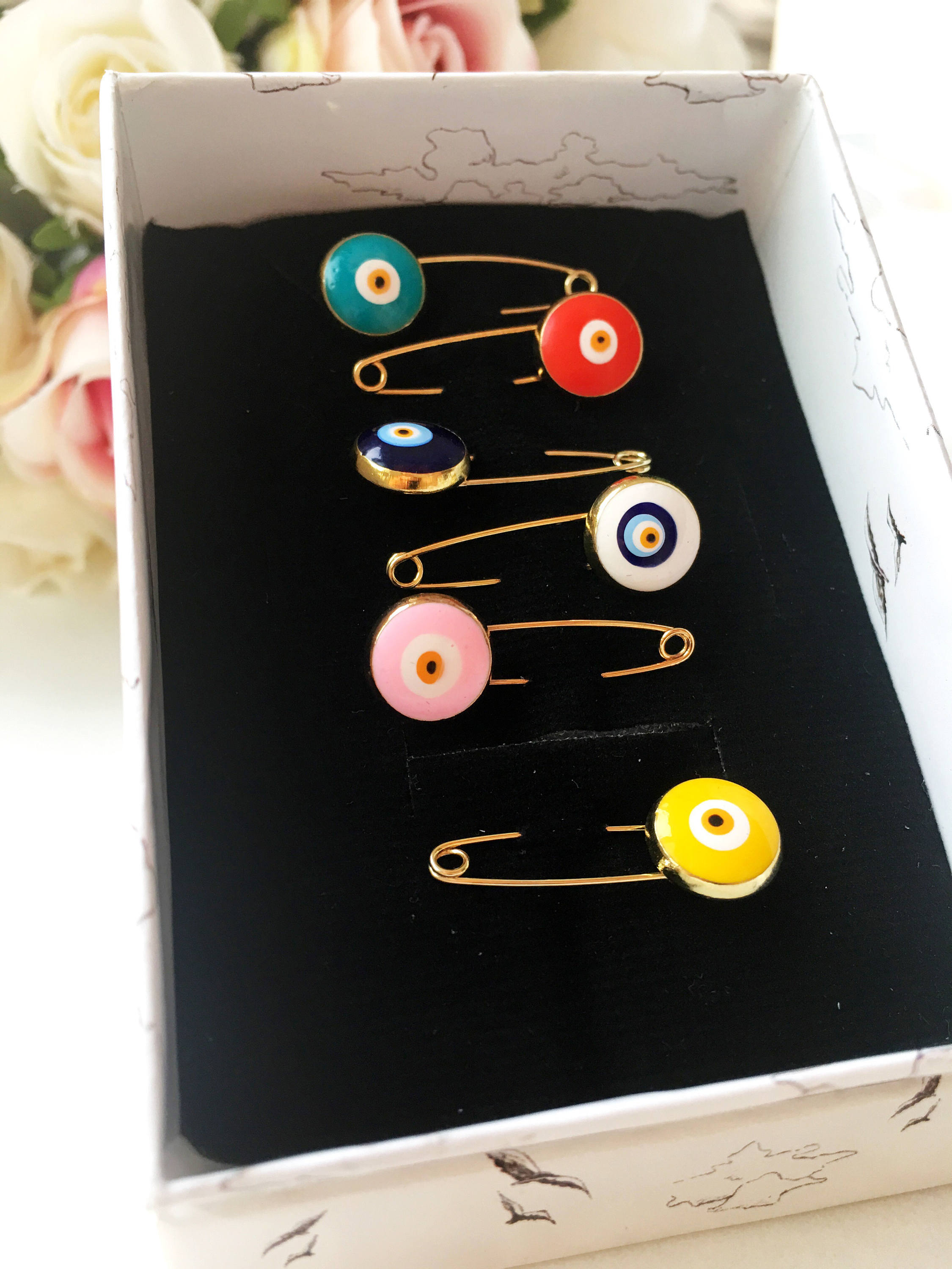 Gold plated evil eye safety pin in various colors, designed for baby shower favors and protection for infants.