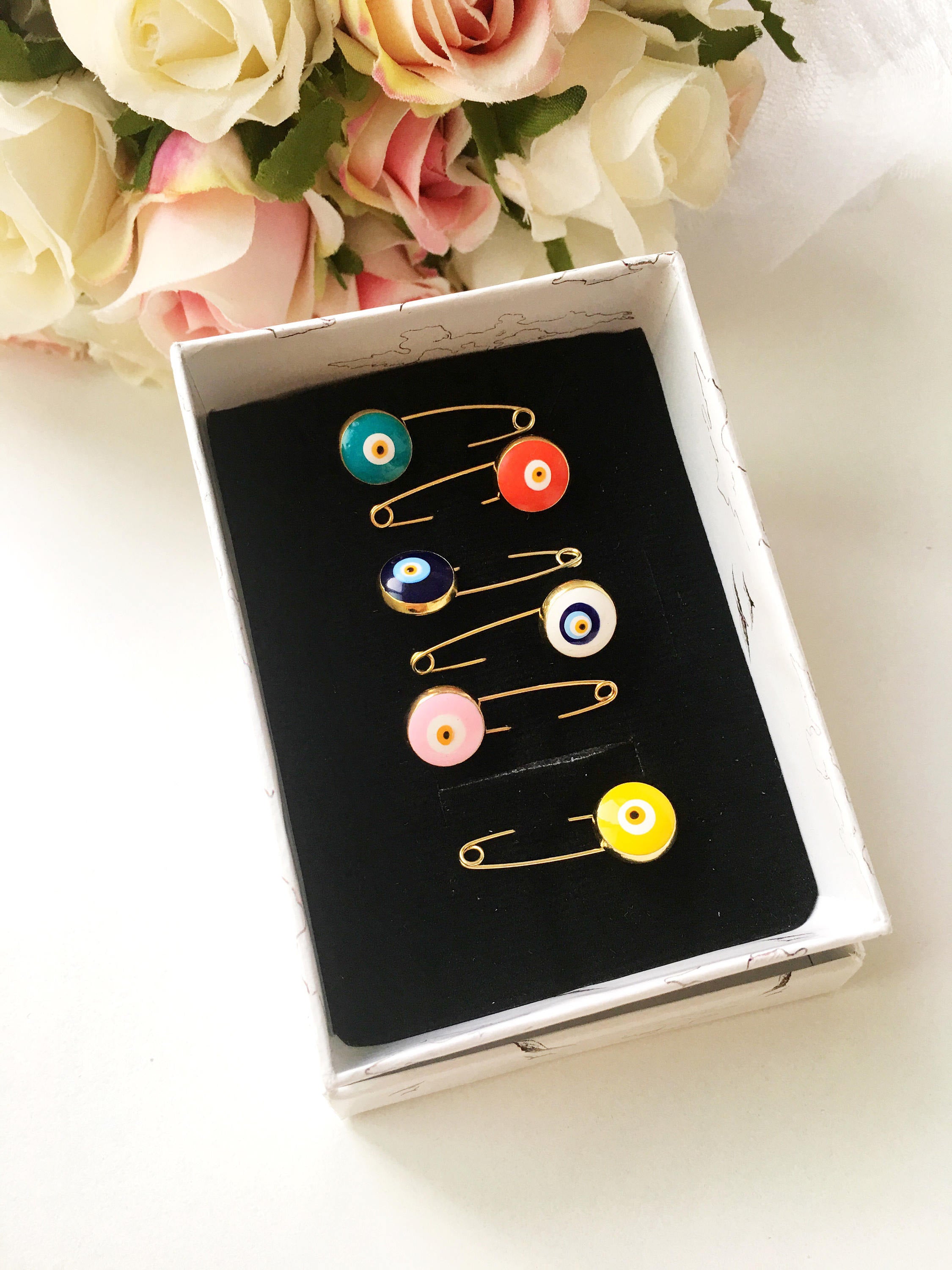 Gold plated evil eye safety pin in various colors, designed for baby shower favors and protection for infants.